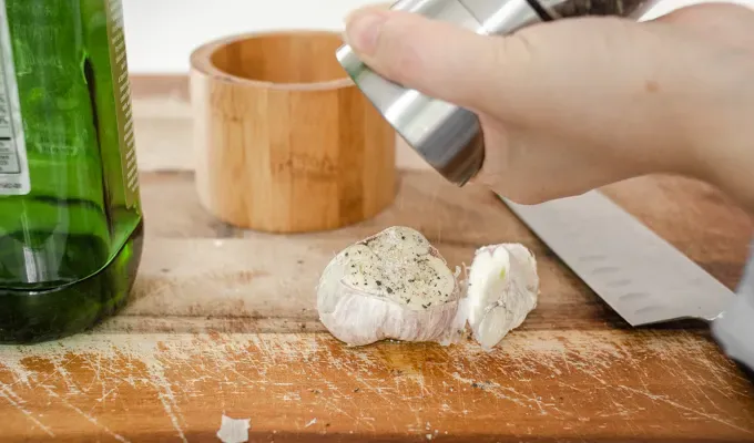 Grating pepper on top of the head of garlic.' title='How to Roast Garlic Without Aluminum Foil