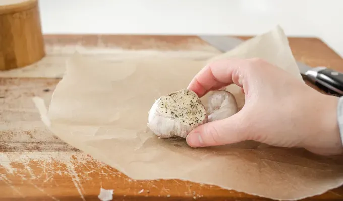 Putting a head of garlic on some parchment paper.' title='How to Roast Garlic Without Aluminum Foil
