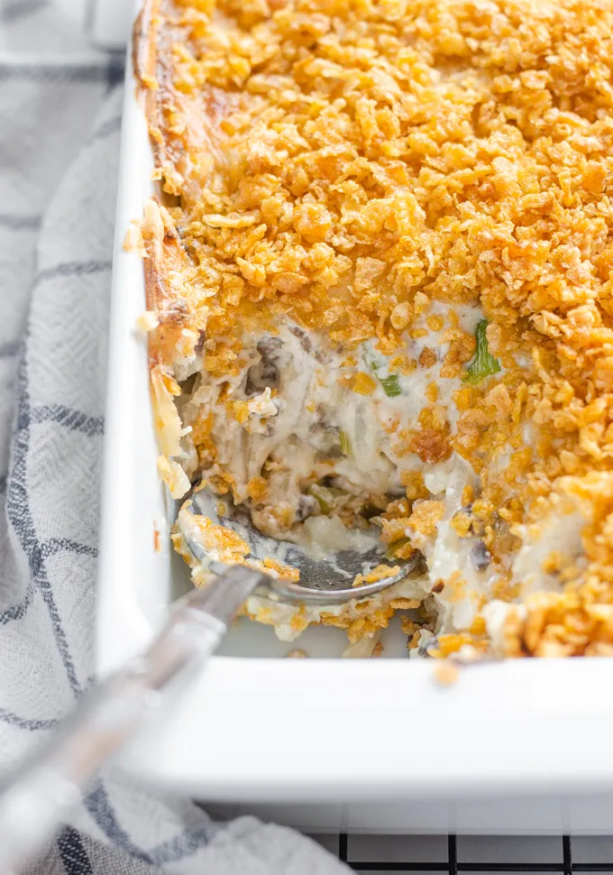The baked gluten free cheesy potatoes (AKA funeral potatoes) in a white casserole dish on top of a wire cooling rack with a scoop taken out.' title='Gluten Free Cheesy Potatoes