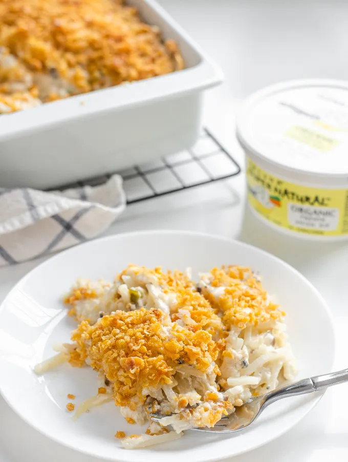 A plate of gluten free cheesy potatoes (AKA funeral potatoes) with the casserole dish in the background.' title='Gluten Free Cheesy Potatoes