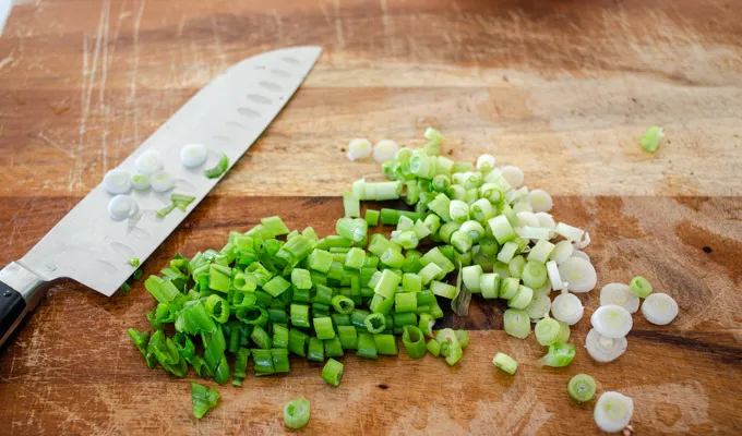 Chopping the green onions on a wooden cutting board.' title='Gluten Free Cheesy Potatoes
