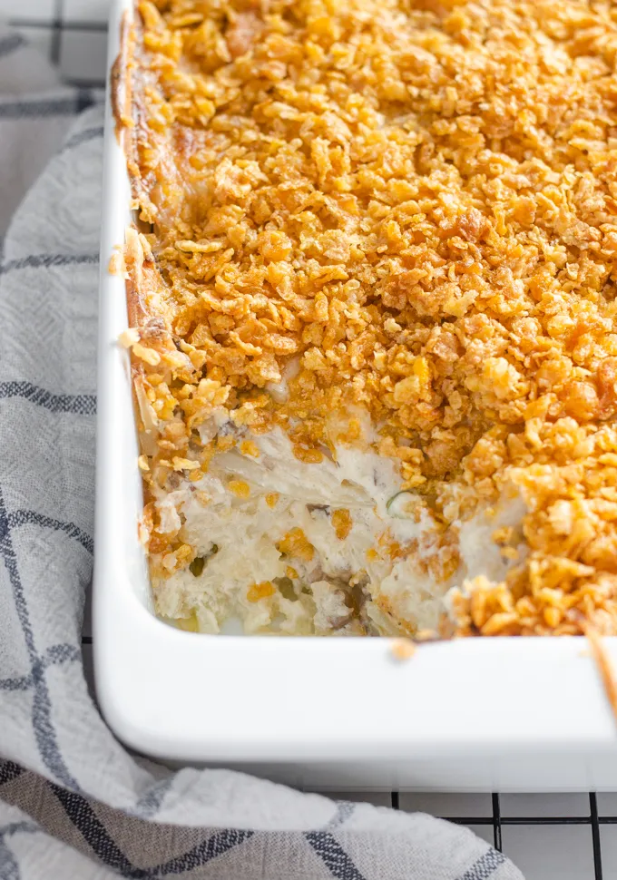 The baked gluten free cheesy potatoes (AKA funeral potatoes) in a white casserole dish on top of a wire cooling rack with a scoop taken out.' title='Gluten Free Cheesy Potatoes