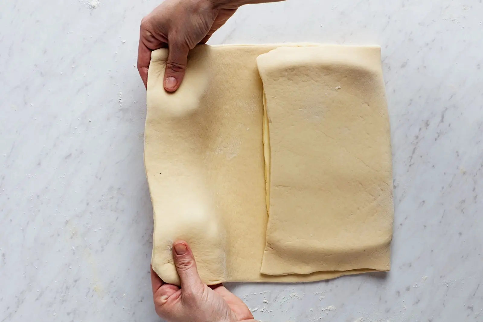 Two hands folding laminated yeast dough for croissants.
