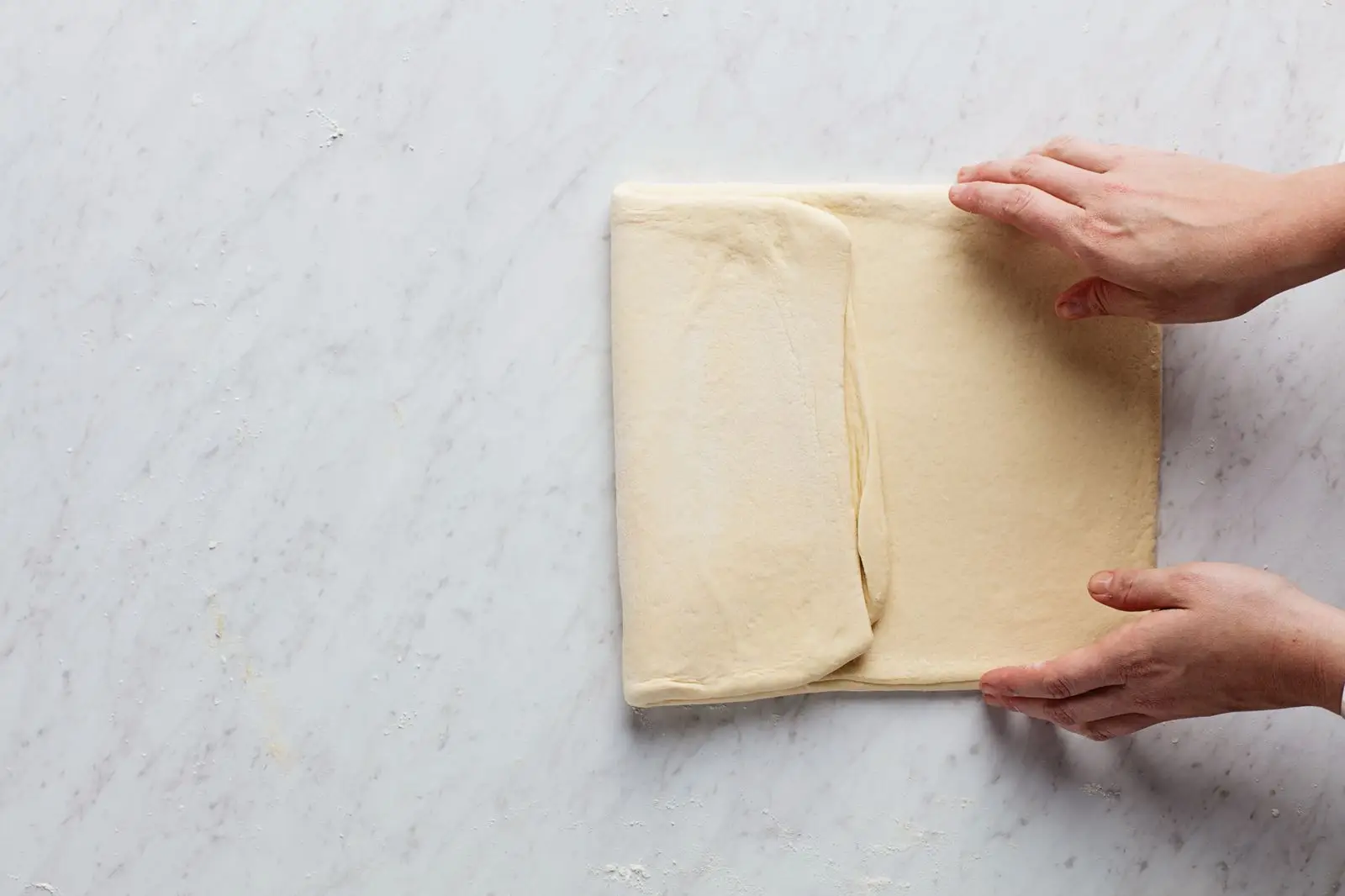 Two hands folding laminated yeast dough for croissants