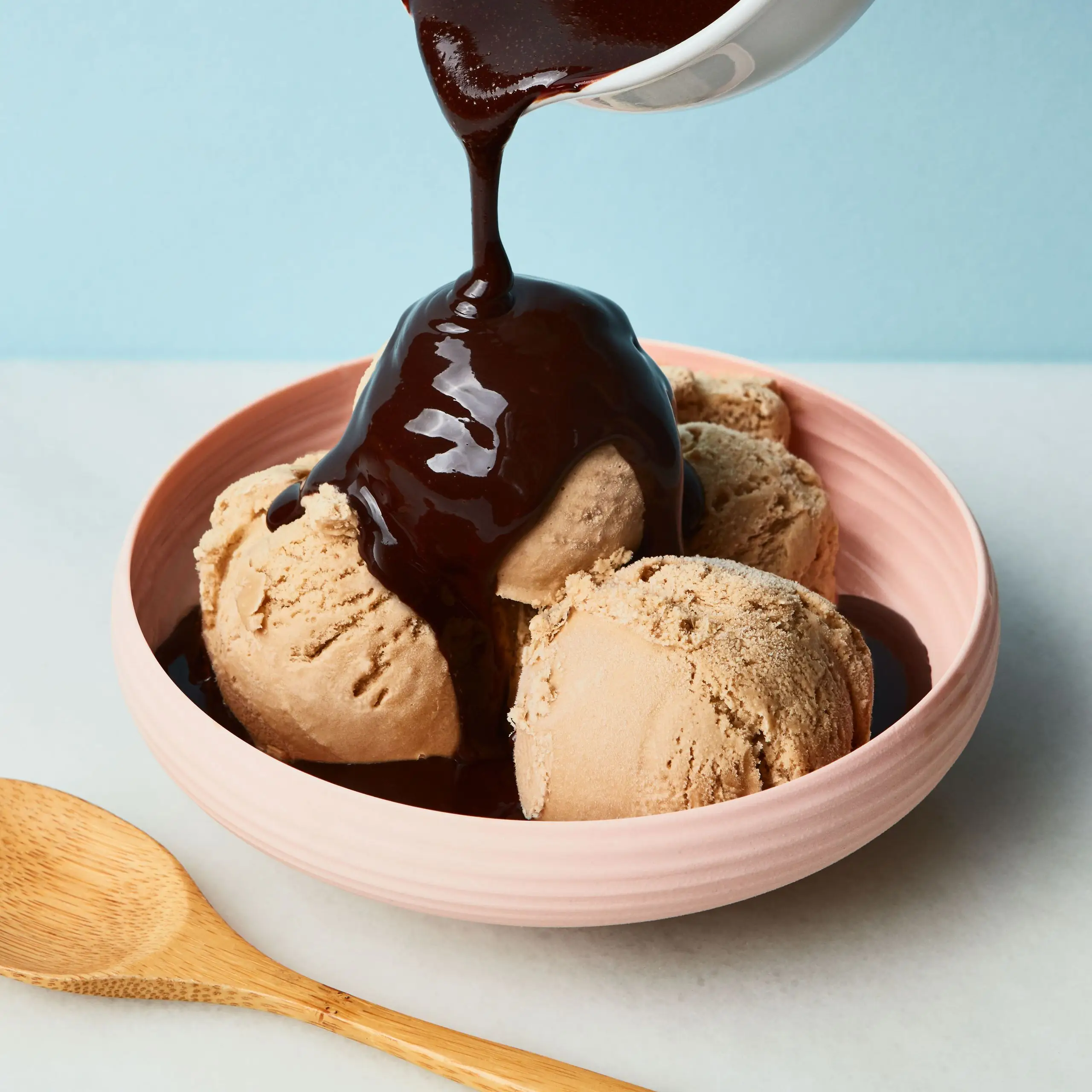 Chocolate syrup being poured onto a bowl of coffee ice cream.