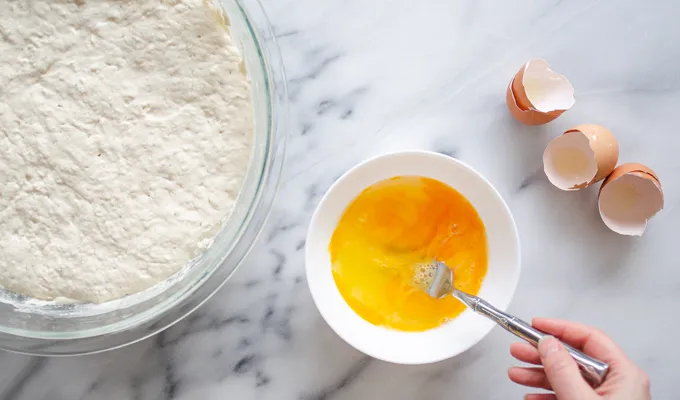 Lightly whisking the eggs in small bowl on a marble surface.' title='The Best Sourdough Pancakes