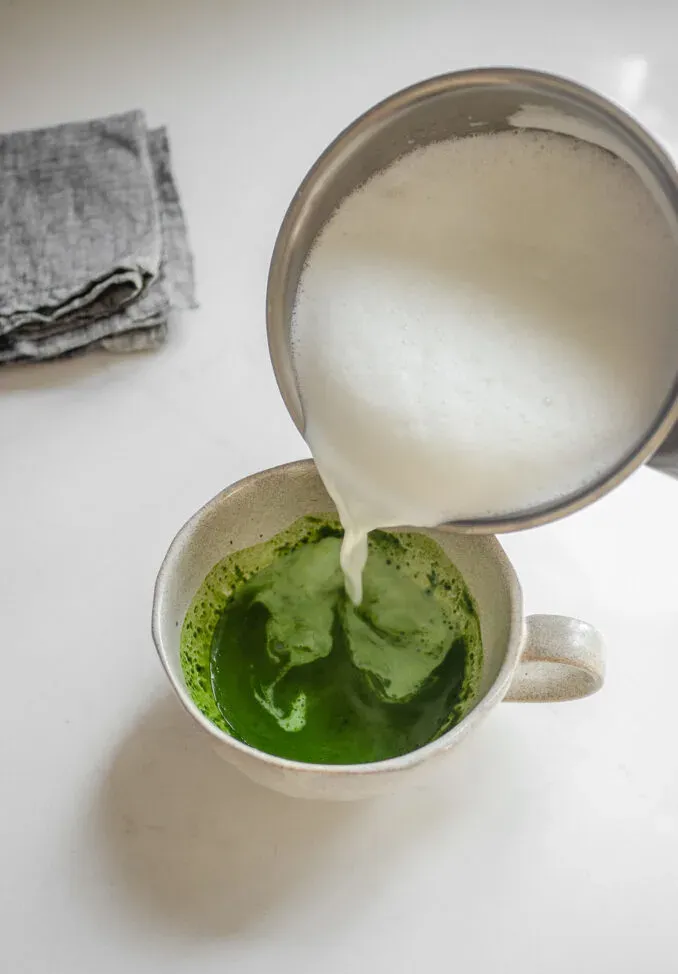 Pouring the frothed milk over the whisked matcha in the mug.' title='Starbucks Hot Matcha Green Tea Latte Recipe