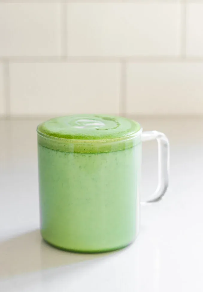 Starbucks copycat matcha green tea latte in a clear glass mug on a white countertop with subway tiles in the background.' title='Starbucks Hot Matcha Green Tea Latte Recipe