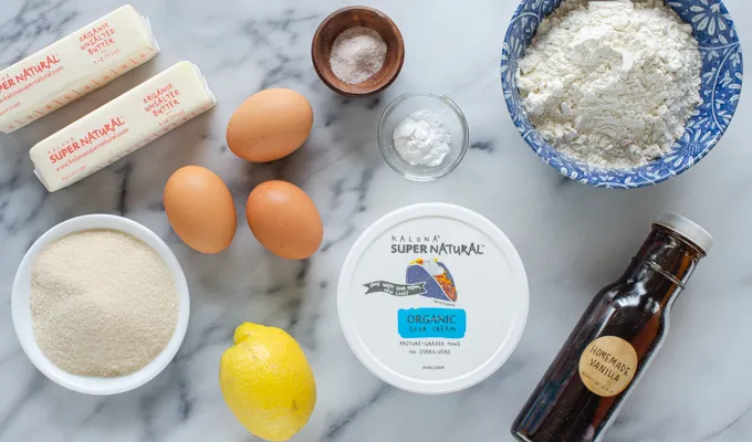 All of the ingredients for a sour cream pound cake loaf laid out on a marble surface.' title='Sour Cream Pound Cake Loaf