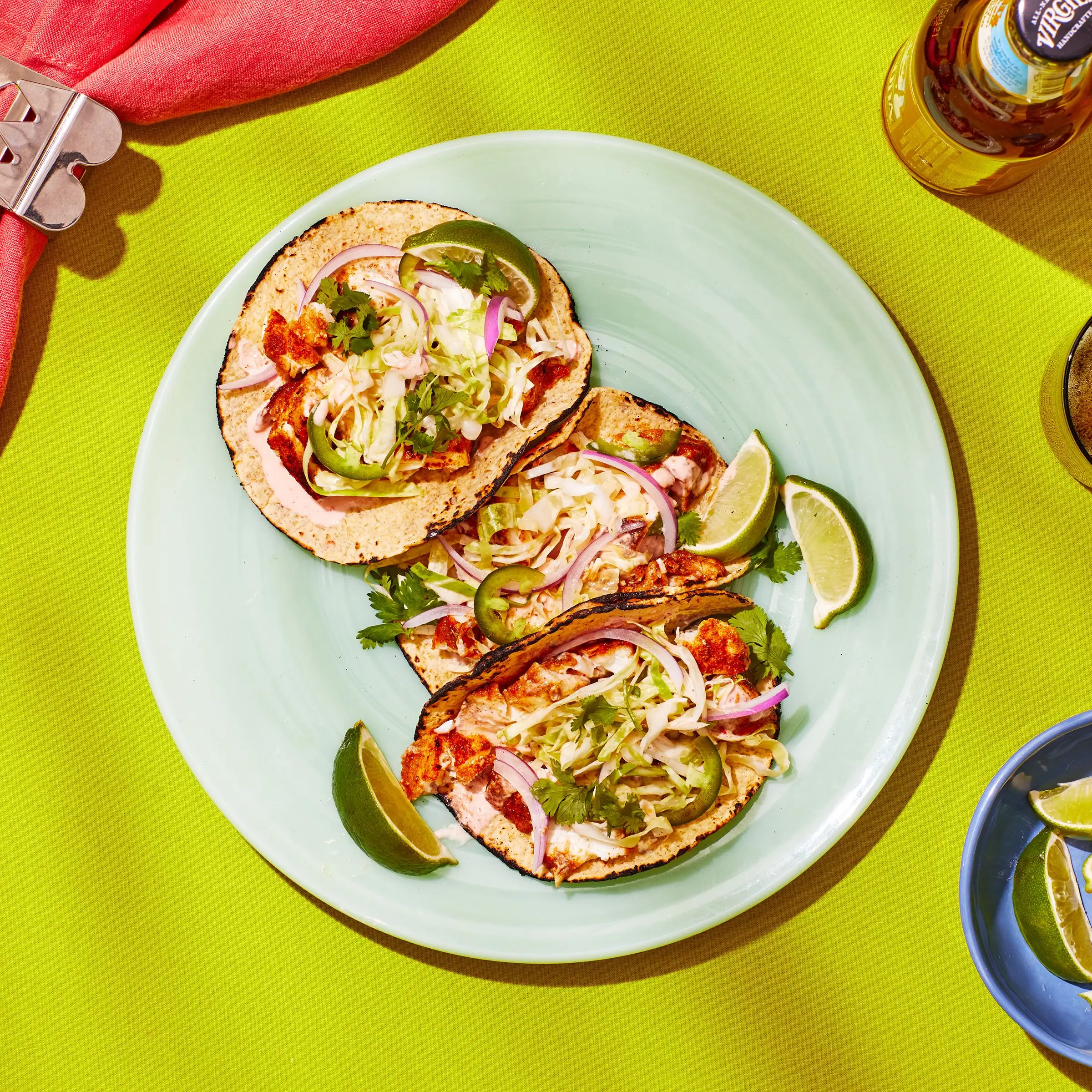 Plate of three fish tacos on a lime green table.