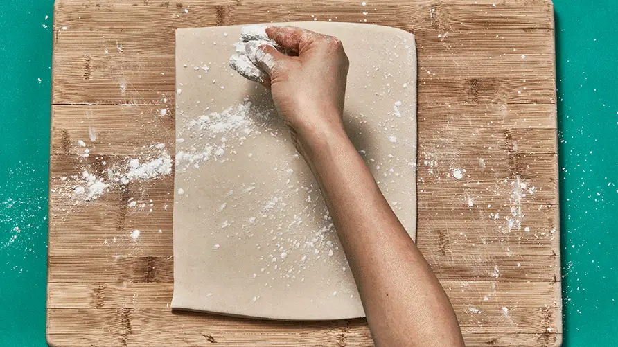 A GIF of udon dough being dusted with flour and sliced into noodles.