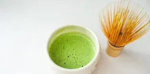 A stone bowl with frothy matcha and a bamboo whisk off to the side.' title='BEST Organic Matcha Powder Review