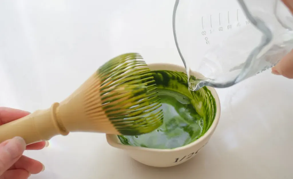 Whiskingg the matcha with hot water in a small spouted bowl to make matcha milk tea.' title='How to Make Matcha Milk Tea with Boba