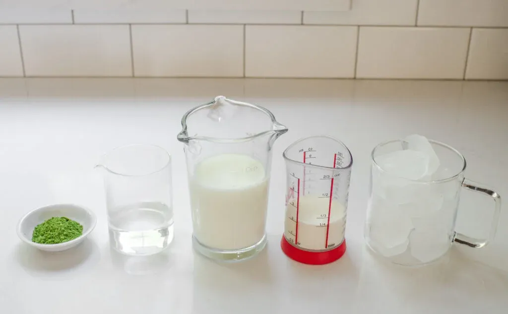 All of the ingredients needed to make matcha milk tea laid out on a white countertop.' title='How to Make Matcha Milk Tea with Boba