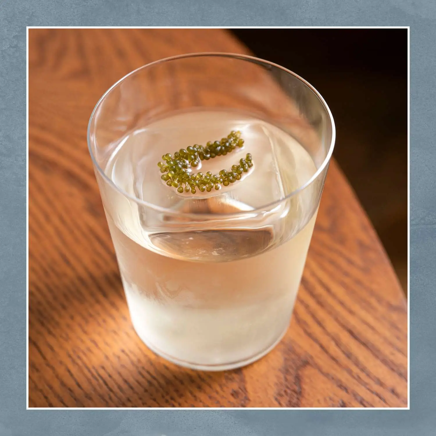 Clarified milk punch with giant ice cube and seaweed garnish, shot on wooden table