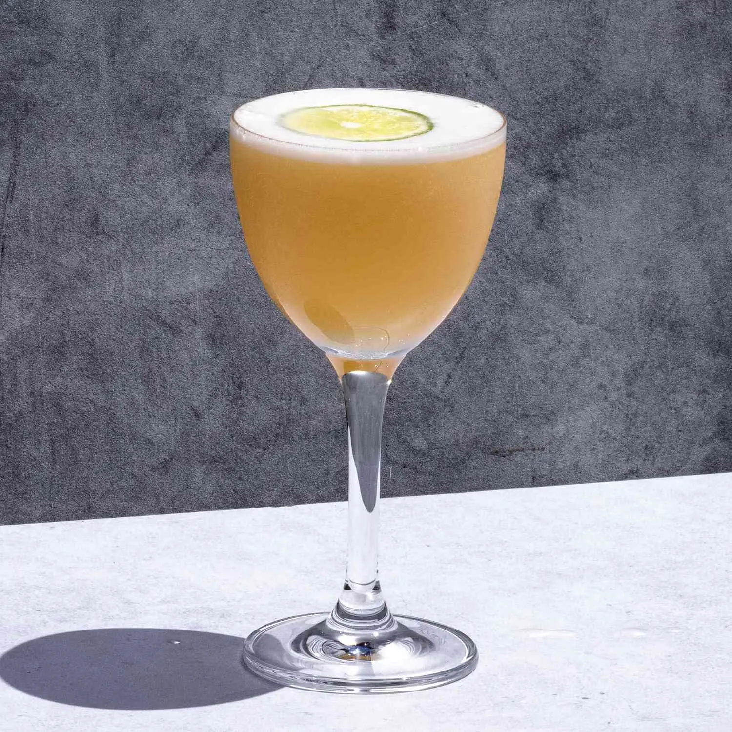 Winter Daiquiri, pale orange, in stemmed Nick & Nora glass, with lime wheel floating on top