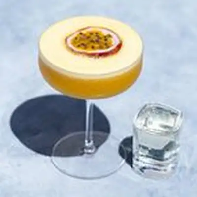 Porn Star Martini, bright orange, filled to the brim in a coupe glass, with half a passion fruit floating as garnish and a shot glass of sparkling wine next to it