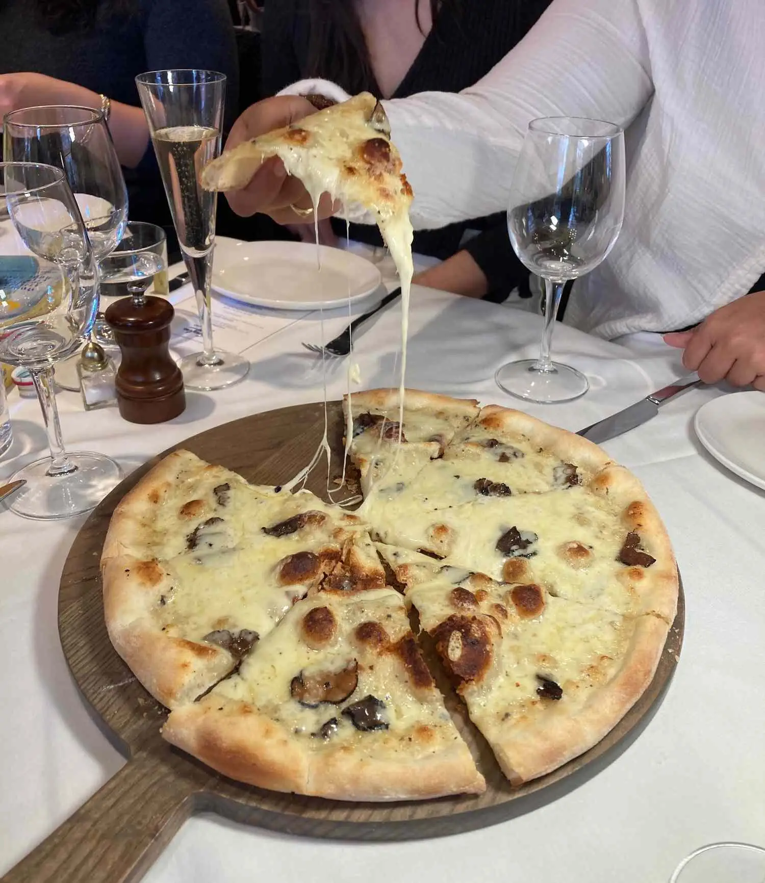 Cheese pull of Cacio e pepe Champagne pizza on wooden pizza peel
