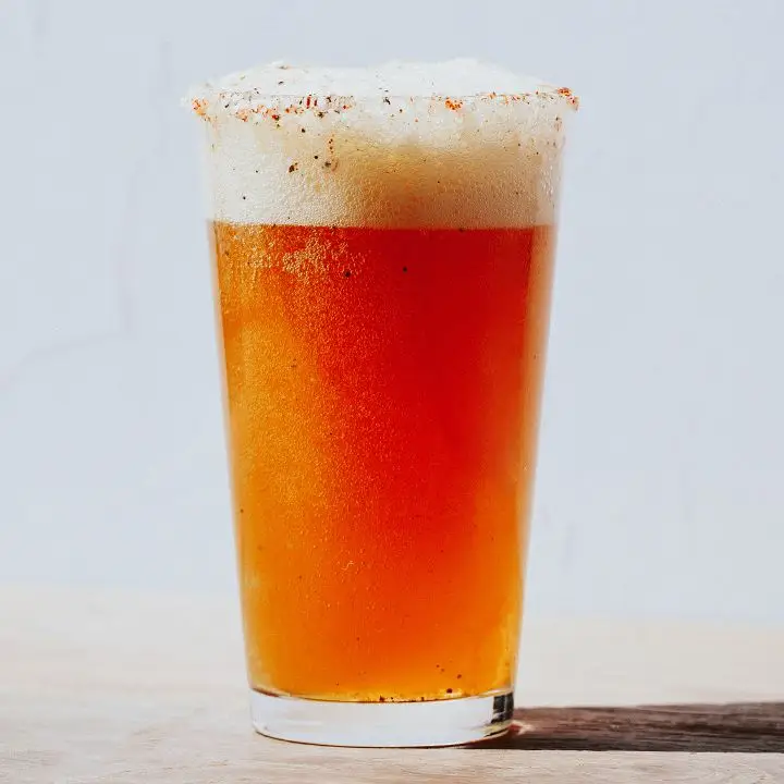 Michelada in pint glass with spicy salt rim, on white background