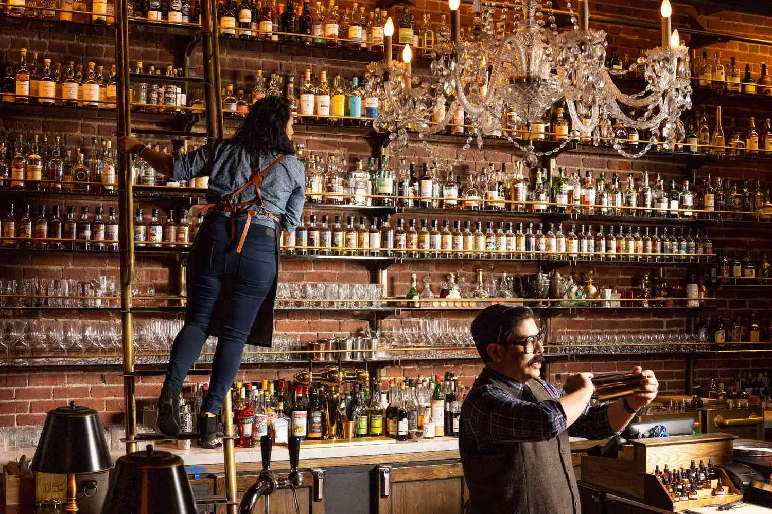 Interior bar of Multnomah Whiskey Library with person shaking cocktail and another on a ladder looking at bottle shelves