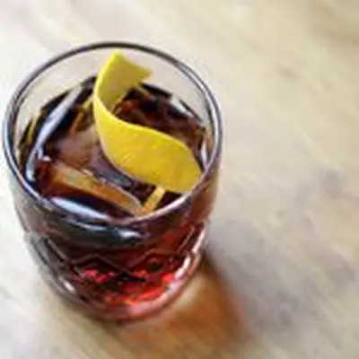 Night Tripper bourbon cocktail served in rocks glass with large ice cube and lemon twist on wooden table