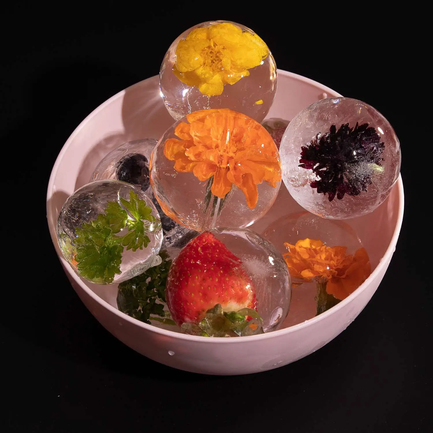 Perfectly clear sphere ice with flowers, fruits, and herbs frozen inside