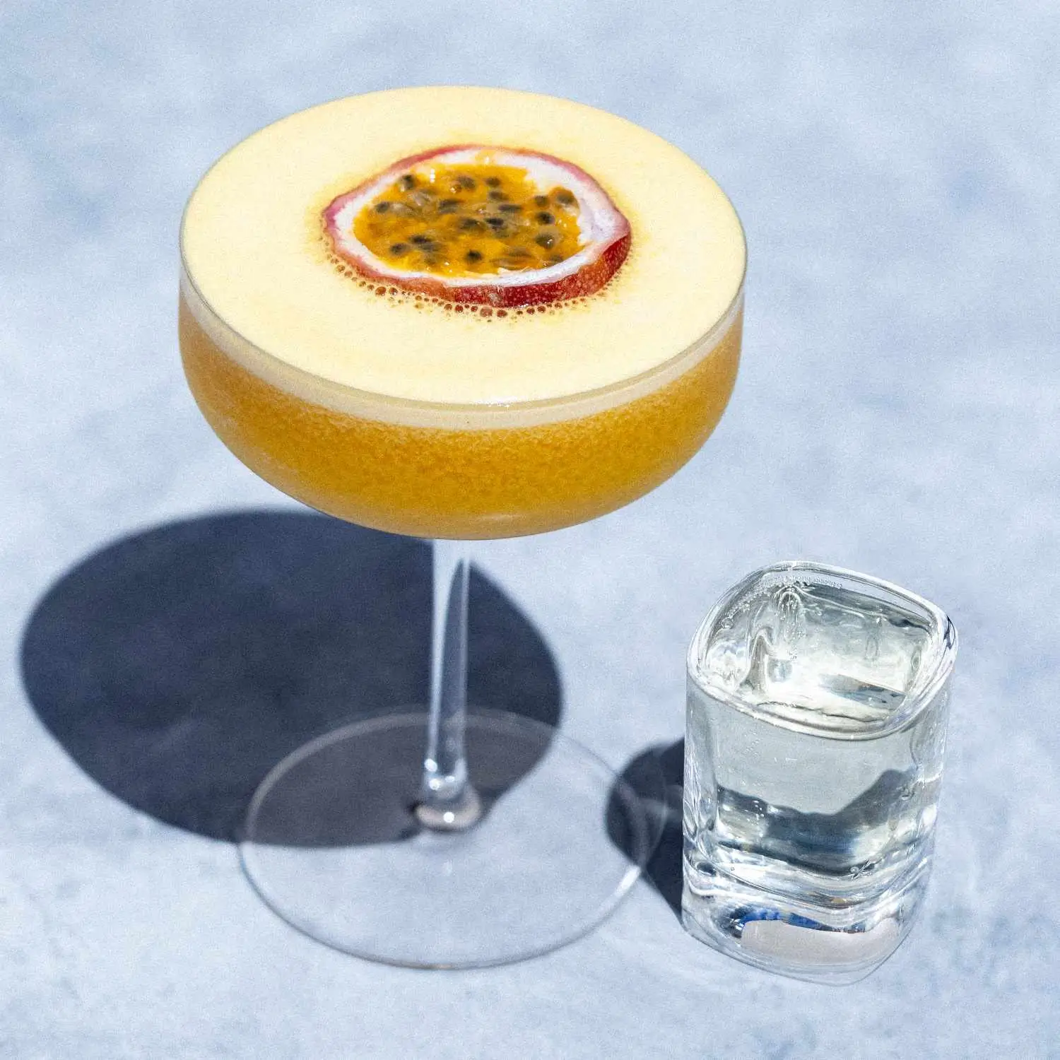 Porn Star Martini, bright orange, filled to the brim in a coupe glass, with half a passion fruit floating as garnish and a shot glass of sparkling wine next to it