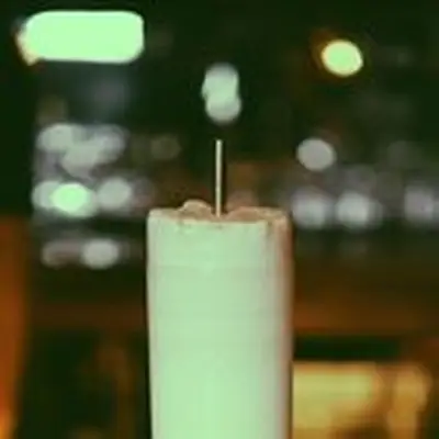 Close-up of Ramos Melon Fizz cocktail with heavy foam and metal straw, shot in Collins glass