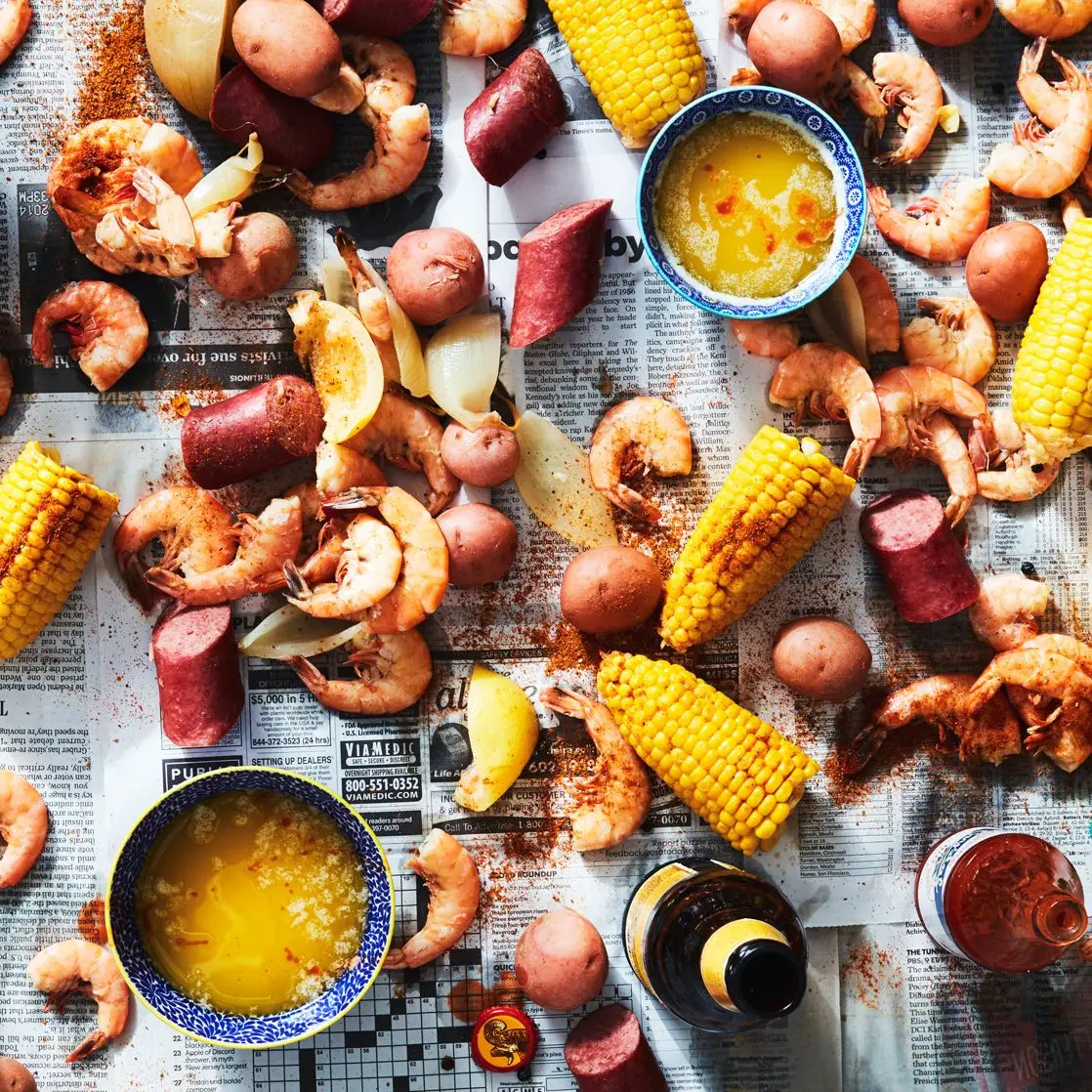 A LowCountry seafood boil of shrimp corn sausages and potatoes scattered on a newspapercovered table.