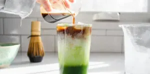 Pouring a shot of espresso on top of the milk and cream in the glass.' title='Matcha Coffee Recipe