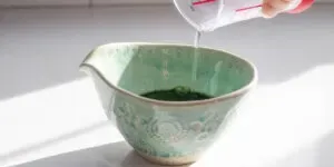 Pouring water on top of matcha and sugar in a small bowl.' title='Matcha Coffee Recipe