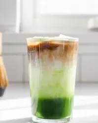 A 12 ounce glass of matcha coffee on a sunny white countertop with a white backsplash in the background' title='Matcha Coffee Recipe