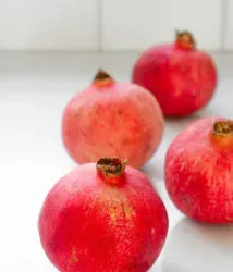 Whole pomegranates on a white countertop.' title='How to Remove Seeds from a Pomegranate