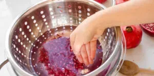 A bowl of water with a colander inside and pomegranate arils in it.' title='How to Remove Seeds from a Pomegranate
