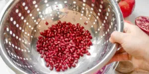 Lifting the colander and pomegranate seeds out of the bowl.' title='How to Remove Seeds from a Pomegranate