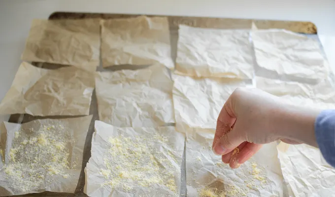 Sprinkling cornmeal on parchment paper to prevent the English muffins from sticking.' title='Sourdough English Muffins