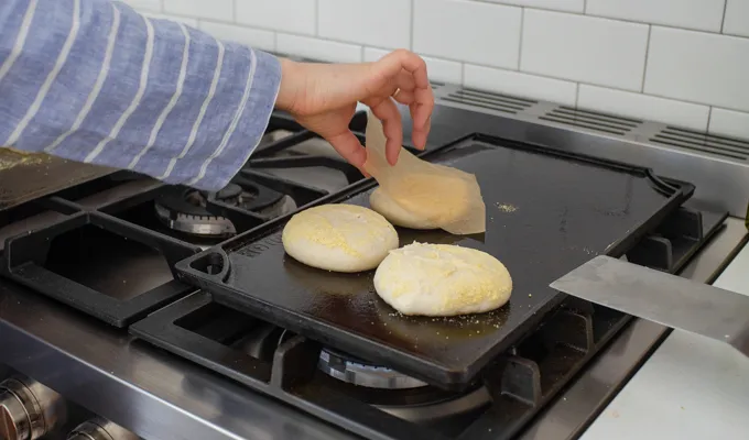 Transferring the risen sourdough English muffins to a preheated cast iron griddle.' title='Sourdough English Muffins