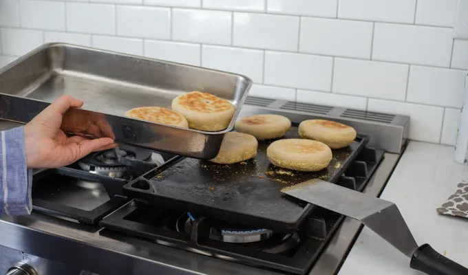 Transferring to a pan to finish baking in the oven.' title='Sourdough English Muffins
