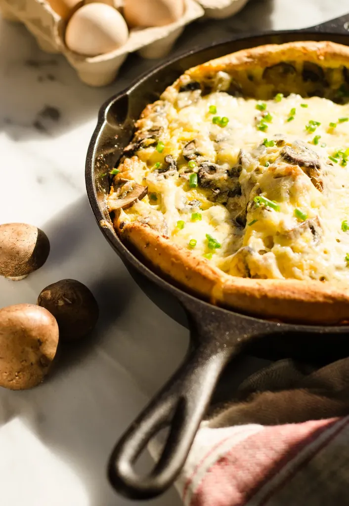 A pan of savory Dutch baby with eggs in the background and a tea towel in the foreground.' title='Savory Dutch Baby Puff Pancake