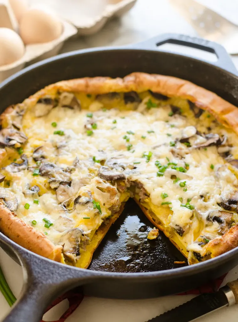 A pan of savory Dutch baby with eggs in the background and a tea towel in the foreground.' title='Savory Dutch Baby Puff Pancake