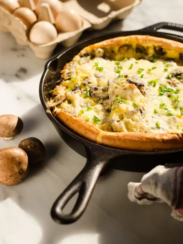 A pan of savory Dutch baby with eggs in the background and a tea towel in the foreground.' title='Savory Dutch Baby Puff Pancake