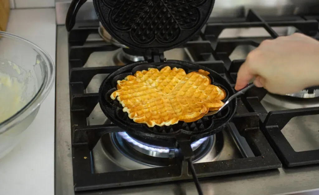 Cooking sourdough discard waffles in a cast iron waffle maker.' title='Sourdough Discard Waffles Recipe
