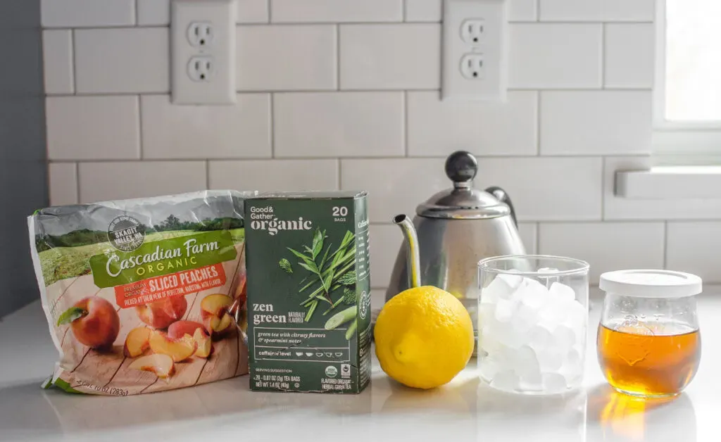 All of the ingredients needed to make a peach green tea lemonade (Starbucks Copycat) laid out on a white counter.' title='Starbucks Peach Green Tea Lemonade Recipe