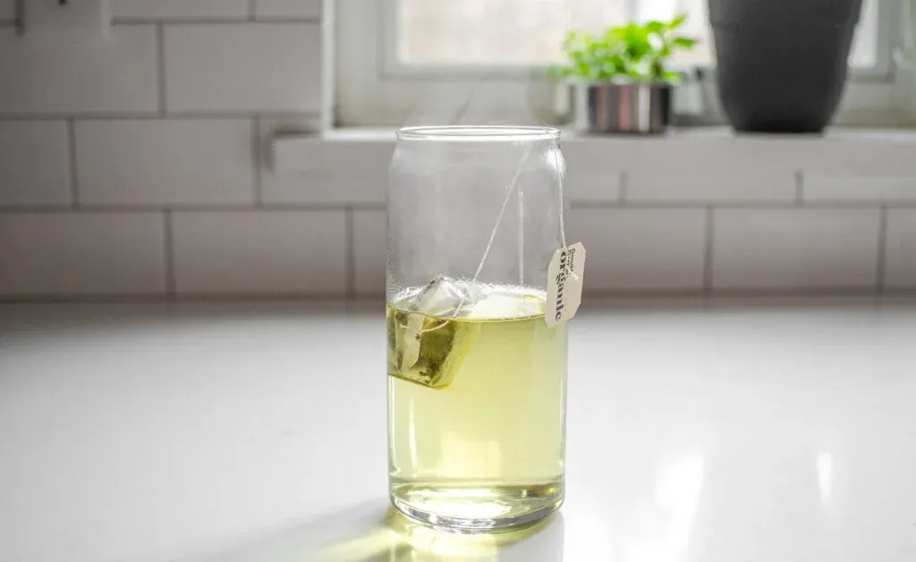 AA tea bag and hot water in a drinking glass on a white countertop.' title='Starbucks Peach Green Tea Lemonade Recipe
