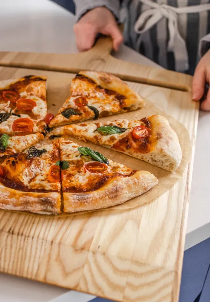 Removing the cooked sourdough pizza from the oven onto a cutting board.' title='Sourdough Pizza Crust Recipe