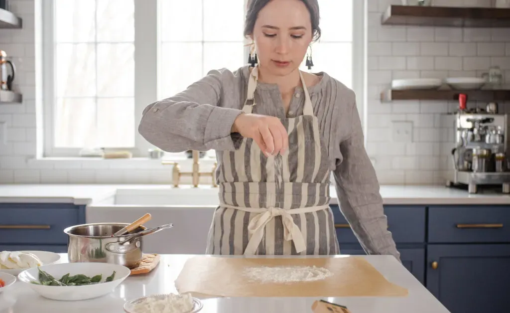 Dusting a piece of parchment paper with flour in preparation for shaping the sourdough pizza crust. ' title='Sourdough Pizza Crust Recipe