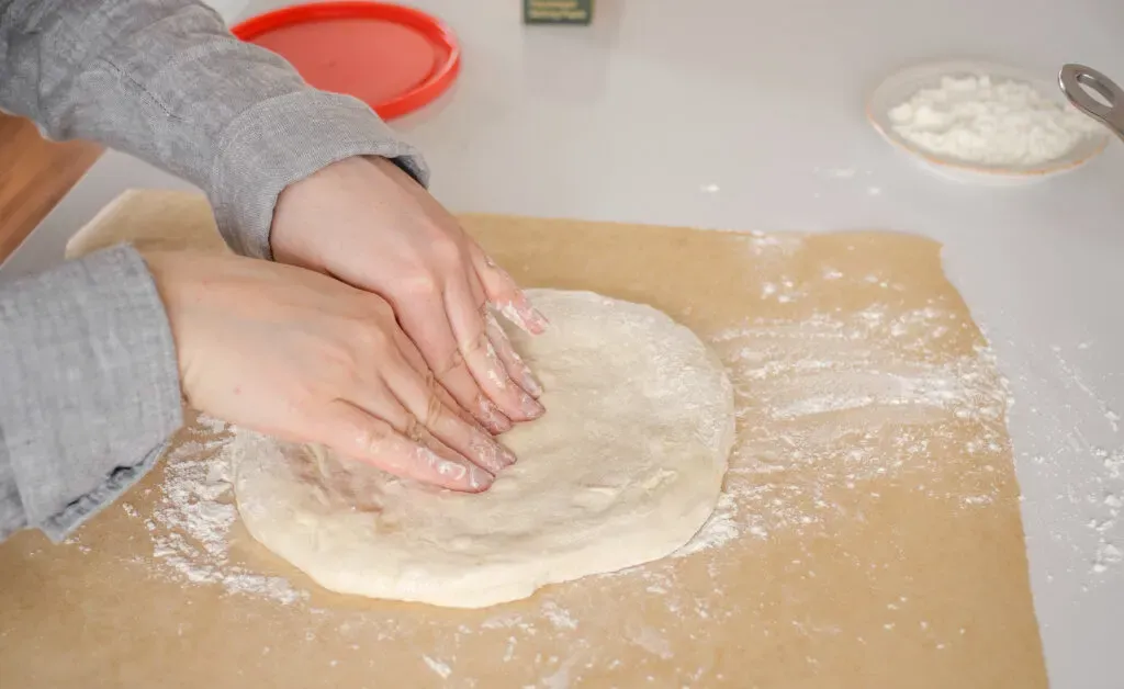 Shaping the sourdough pizza dough on a sheet of floured parchment paper.' title='Sourdough Pizza Crust Recipe