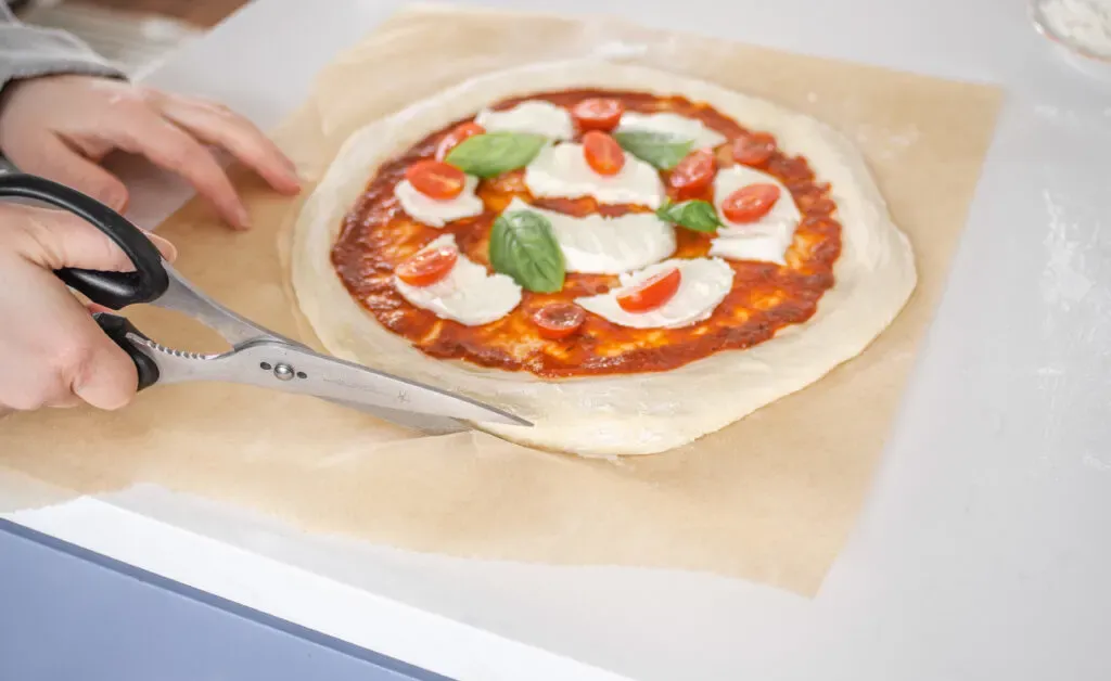 Trimming the parchment paper with scissors so it doesn’t burn.' title='Sourdough Pizza Crust Recipe