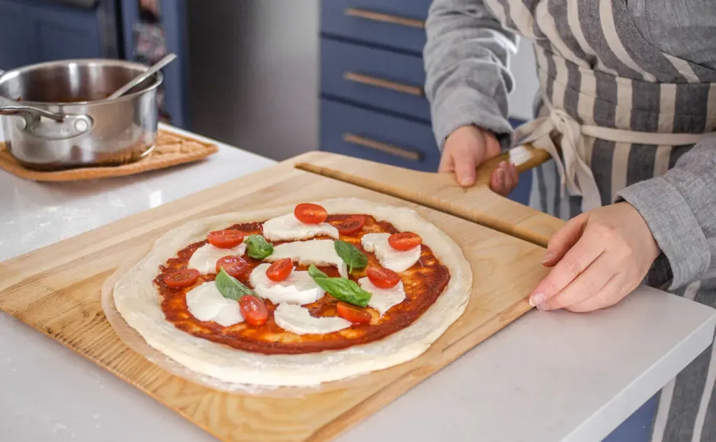 Transferring the topped sourdough pizza crust onto a pizza peel to transfer to the oven.' title='Sourdough Pizza Crust Recipe