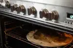 Placing a pizza stone in an oven to preheat for baking the sourdough pizza crust.' title='Sourdough Pizza Crust Recipe